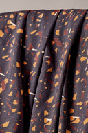 Tissu viscose Candy Rock anthracite à imprimé confettis graphiques caramel et rouille, drapé sur l'accoudoir en bois d'une chaise vintage.