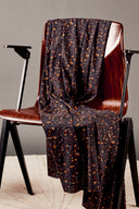 Tissu viscose imprimé confettis façon terrazzo anthracite à éclats orange et caramel, drapé sur une chaise vintage en bois.