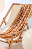 Tissu Domino moutarde drapé sur une chaise longue pliante en bois à assise écrue, avec des ballons blancs en arrière-plan.