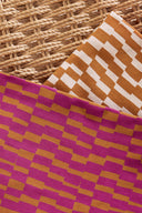 Tissus Domino aux motifs graphiques en escalier dans plusieurs coloris, moutarde et écru puis fuchsia et moutarde, posés sur une surface tressée.
