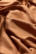 Tissu Flake caramel suspendu à une tringle noire, en plis amples et aériens sur un fond clair.