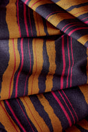 Tissu viscose Flow à rayures irrégulières moutarde, marine et fuchsia, drapé avec des brins d'herbe de pampa séchée sur fond beige.