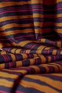 Tissu Flow moutarde et marine plié, avec un bol en métal doré contenant des boutons marron et noirs, près d'objets en céramique en forme d'œufs ivoire.