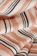 Tissu viscose Flow écru à rayures irrégulières terracotta et marine, drapé sur un support en bois, avec des brins d'herbe de pampa séchée à proximité.