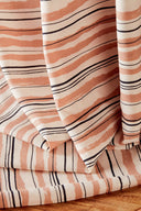 Gros plan sur les plis du tissu Flow écru laissant apparaître le détail des rayures terracotta et marine irrégulières.
