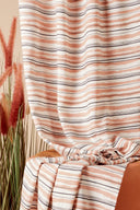 Vue rapprochée du tissu Flow écru superposé en plusieurs plis, montrant la répétition du motif rayé terracotta et marine.