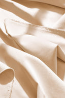 Tissu gabardine légère écru drapé en plis fluides sur l'angle d'un socle blanc.