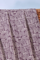 Tissu Hopscotch mauve drapé sur une chaise longue pliante en bois à assise écrue, avec des ballons orange en arrière-plan.