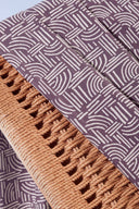 Tissu Hopscotch mauve à motif graphique de traits entrelacés écru, en plis contre le cannage tressé d'une chaise.