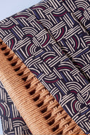 Tissu Hopscotch marine à motif graphique de traits entrelacés écru, bordeaux et bleu, en plis contre le cannage tressé d'une chaise.