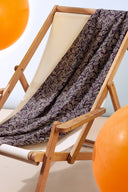 Tissu Hopscotch marine drapé sur une chaise longue pliante en bois à assise écrue, avec des ballons orange en arrière-plan.