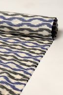 Tissu écru enroulé en rouleau, montrant le motif à chevrons bleu et anthracite façon ikat sur toute la longueur.