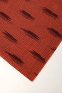 Tissu terracotta enroulé en rouleau, détaillant les traits aubergine façon ikat et la lisière effilochée.