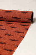 Gros plan sur le tissu terracotta enroulé, montrant le motif de traits aubergine façon ikat sur toute la longueur.