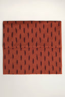 Tissu L'Ikat terracotta plié à plat, motif de traits aubergine façon ikat disposés en rangées verticales sur l'ensemble de la pièce.