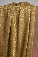 Golden khaki Leony jacquard fabric with a raised woven leopard pattern, draped in folds against a wooden support.