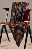Tissu viscose imprimé graphique noir à motifs ronds et rayés gris, beige et orange, drapé sur une chaise vintage en bois.