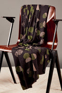 Tissu viscose imprimé graphique noir à motifs ronds et rayés vert olive et rose poudré, drapé sur une chaise vintage en bois.
