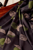 Tissu viscose Jane noir à motif graphique de demi-cercles kaki et rose poudré, drapé sur l'accoudoir en bois d'une chaise vintage.