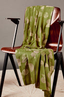 Tissu viscose imprimé graphique vert matcha à larges motifs ronds et rayés beige, drapé sur le dossier et l'assise d'une chaise vintage en bois.