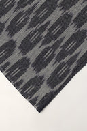 Gros plan sur l'angle plié du voile anthracite, détaillant le motif abstrait façon ikat et la lisière effilochée.