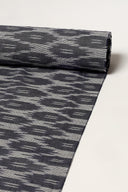 Voile de coton anthracite enroulé en rouleau, montrant le motif abstrait façon ikat sur toute la longueur.