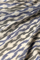 Tissu L'Ikat écru à chevrons bleu et anthracite façon ikat, drapé en plis diagonaux.