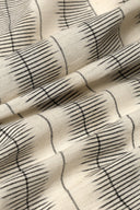 Tissu L'Ikat écru à fines rayures anthracite façon ikat, drapé en plis diagonaux.