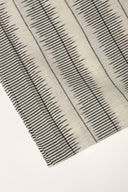 Gros plan sur l'angle plié du tissu écru, détaillant les rayures anthracite façon plumetis et la lisière effilochée.