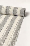 Tissu écru enroulé en rouleau, montrant les rayures anthracite façon ikat sur toute la longueur.