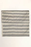 Tissu L'Ikat écru plié à plat, rayures anthracite façon ikat disposées en bandes régulières sur l'ensemble de la pièce.