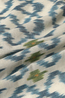 Tissu L'Ikat écru à losanges bleu indigo façon ikat rehaussés de touches vert olive et orange, drapé en plis souples.