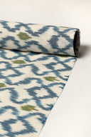 Tissu écru enroulé en rouleau, montrant le motif de losanges bleu indigo façon ikat sur toute la longueur.