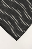 Gros plan sur l'angle plié du tissu anthracite, détaillant les rayures diagonales écru façon ikat et la lisière effilochée.