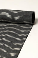 Tissu anthracite enroulé en rouleau, montrant les rayures diagonales écru façon ikat sur toute la longueur.