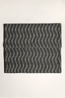 Tissu L'Ikat anthracite plié à plat, motif de rayures ondulées écru façon ikat formant un jeu de losanges sur l'ensemble de la pièce.