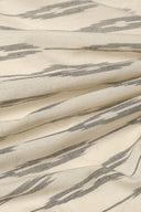 Tissu L'Ikat écru à rayures anthracite façon ikat, drapé en plis diagonaux.