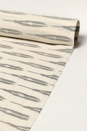 Tissu écru enroulé en rouleau, montrant les rayures anthracite façon ikat sur toute la longueur.