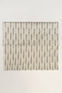 Tissu L'Ikat écru plié à plat, rayures anthracite façon ikat disposées en bandes régulières sur l'ensemble de la pièce.