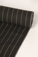 Close-up of the corner of the La Rayure 002 charcoal fabric with fine ecru stripes, highlighting the pattern and the frayed selvedge.