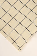 Tissu Le Carreau 002 jaune pâle à petits carreaux marine façon vichy, enroulé en rouleau laissant voir la lisière tissée.