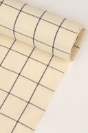 Gros plan sur le coin du tissu Le Carreau 002 jaune pâle à petits carreaux marine façon vichy, mettant en valeur le motif et la lisière effilochée.