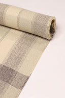 Gros plan sur le coin du tissu Le Carreau 006 écru à carreaux taupe chiné façon tartan, mettant en valeur le motif et la lisière effilochée.