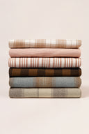 Pile de coupons de tissus de la collection Le Bazaar, motifs carreaux et rayures superposés dans des tons kaki, marine, beige, vert foncé et marron.