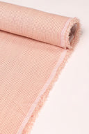 Gros plan sur le coin du tissu Le Carreau 010 rose poudré à fin quadrillage tissé ton sur ton, mettant en valeur le motif et la lisière effilochée.