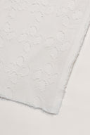Gros plan sur le coin du tissu Le Coton Indien Tissé 001 écru, détaillant le motif floral tissé ton sur ton et la lisière effilochée.