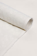 Tissu Le Coton Indien Tissé 001 écru enroulé en rouleau, motif floral tissé en relief visible sur toute la longueur, lisière effilochée apparente.