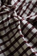 Burgundy and ecru seersucker fabric with a small gingham check, draped in flowing folds revealing the characteristic puckered seersucker texture.