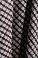Close-up of the textured burgundy and ecru gingham seersucker cotton fabric, draped in tight folds.