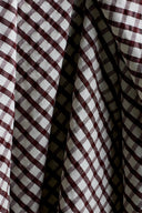 Close-up of the folds of the textured burgundy and ecru gingham seersucker cotton fabric, playing with the light.